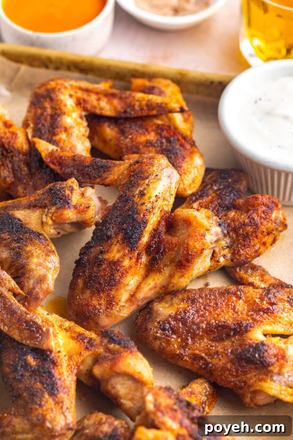 Whole chicken wings on a baking sheet lined with parchment paper next to a ramekin of ranch dressing, ready to be served.
