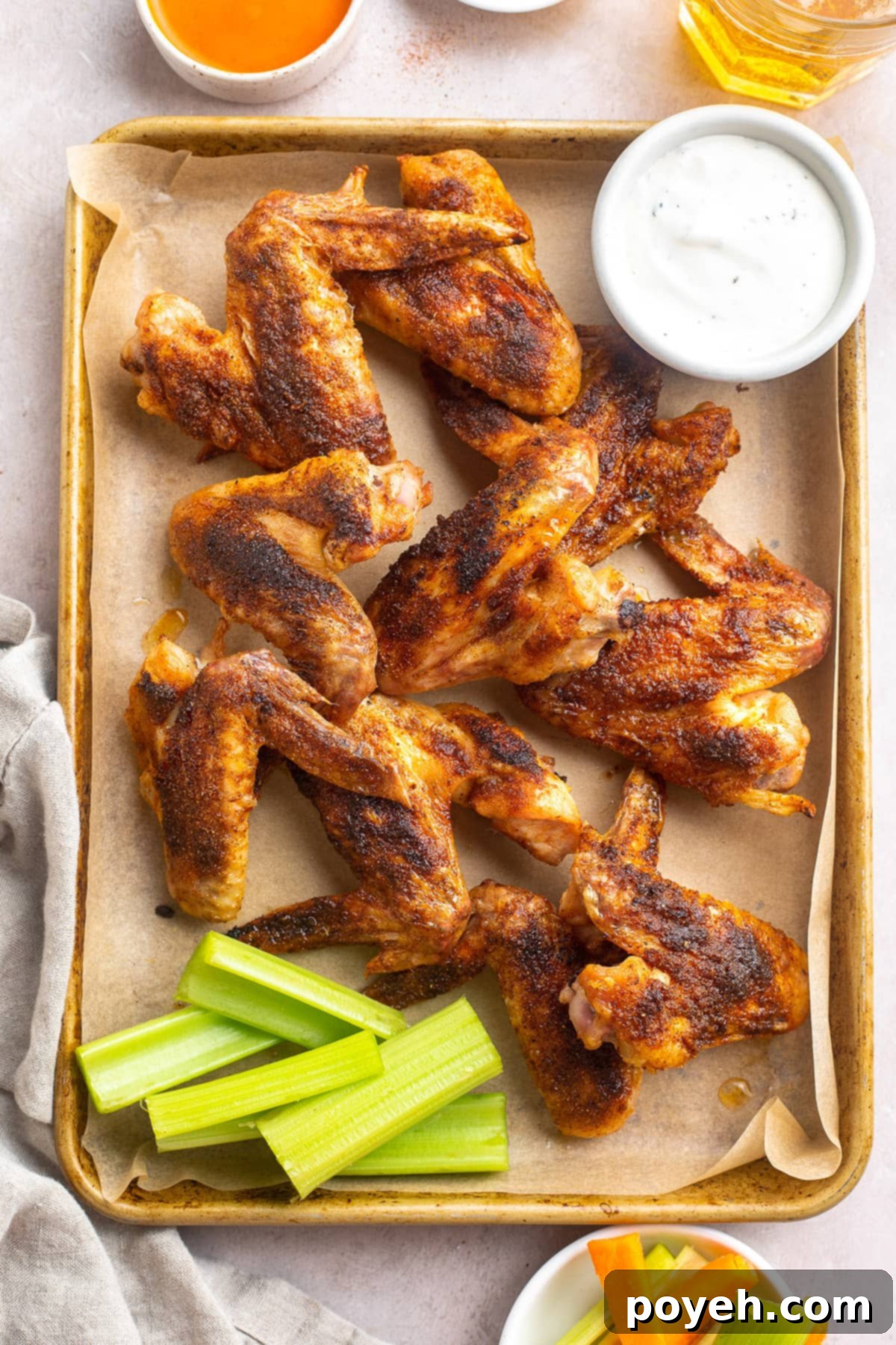 Whole chicken wings on a baking sheet lined with parchment paper next to a ramekin of ranch dressing, glistening and golden.