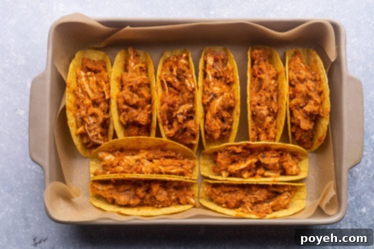 Crunchy taco shells upright in a baking pan and filled with shredded chicken mixture.