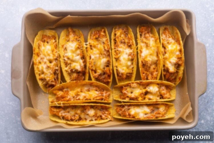 A baking pan filled with 10 baked chicken tacos in crispy taco shells.