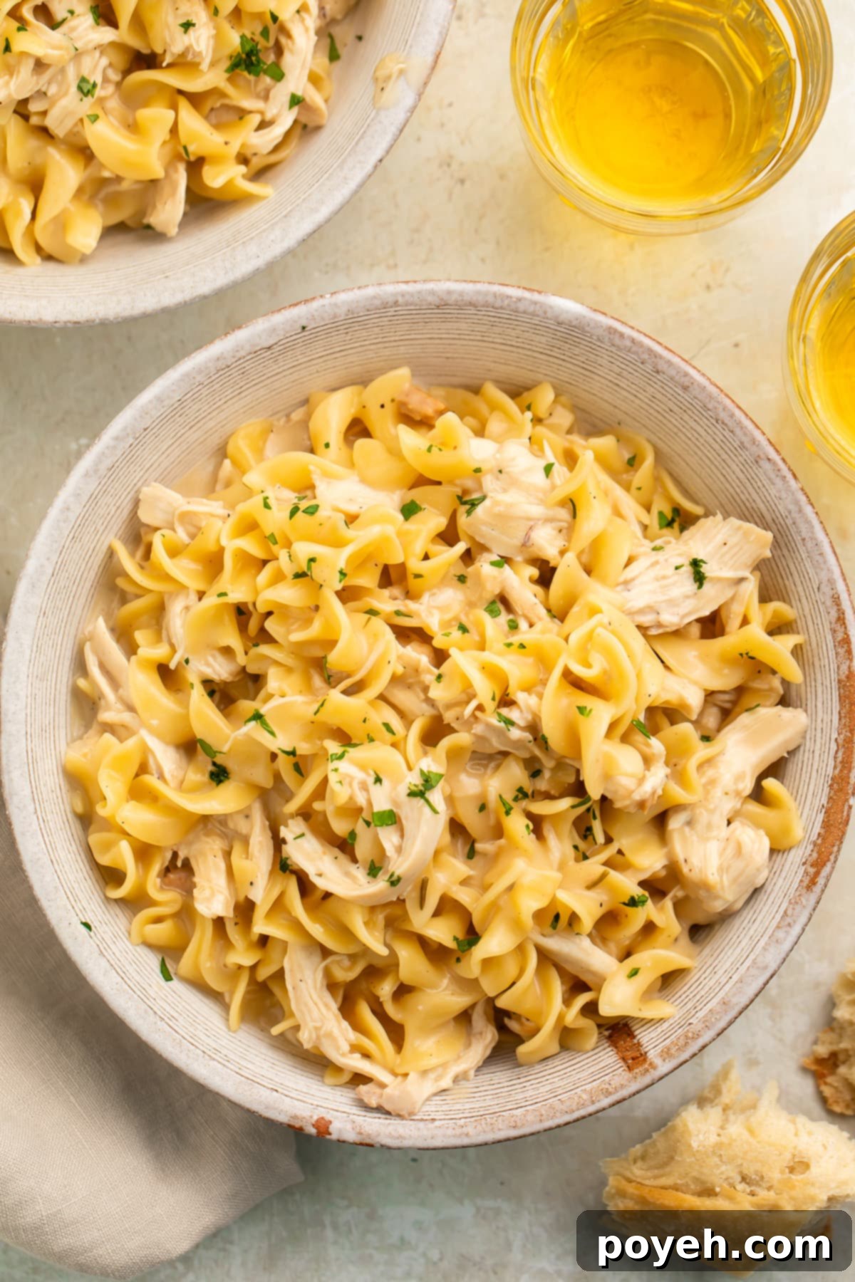 Quick & Cozy Instant Pot Chicken Noodles 3 Overhead view of two bowls of Instant Pot chicken and noodles on a white table top with glasses of white wine.