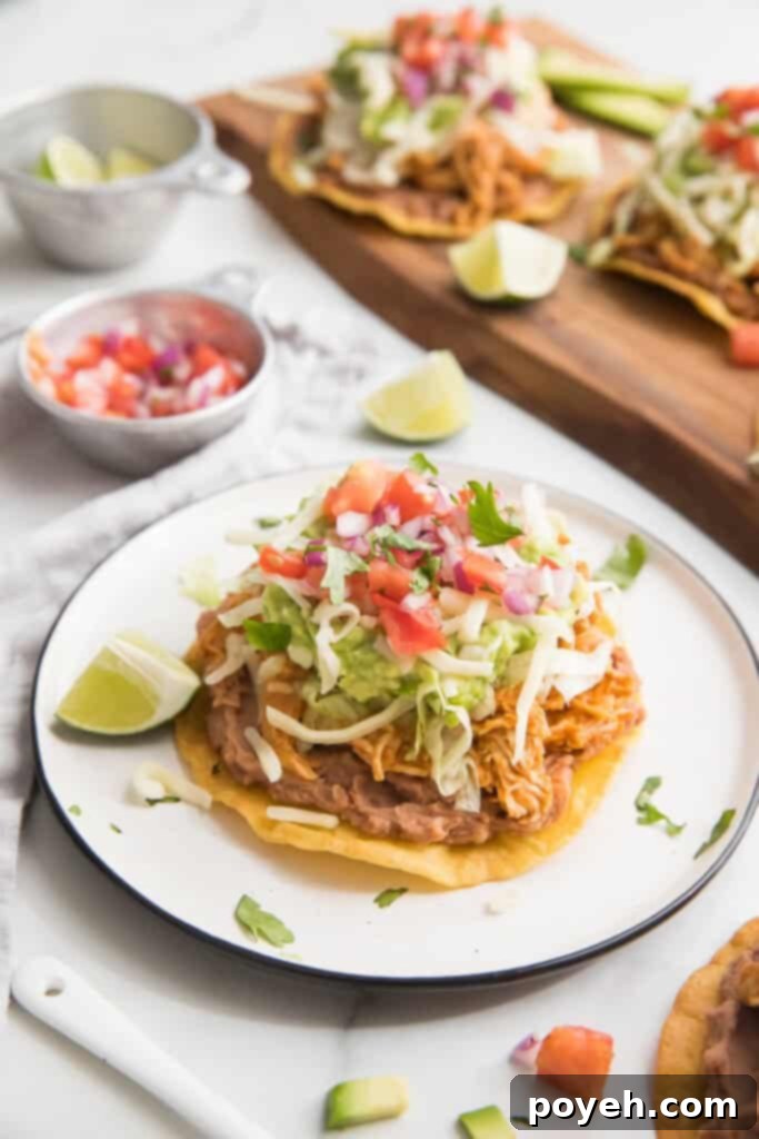 A chicken tostada on a white plate with lettuce, cheese, guacamole and salsa, ready to be eaten