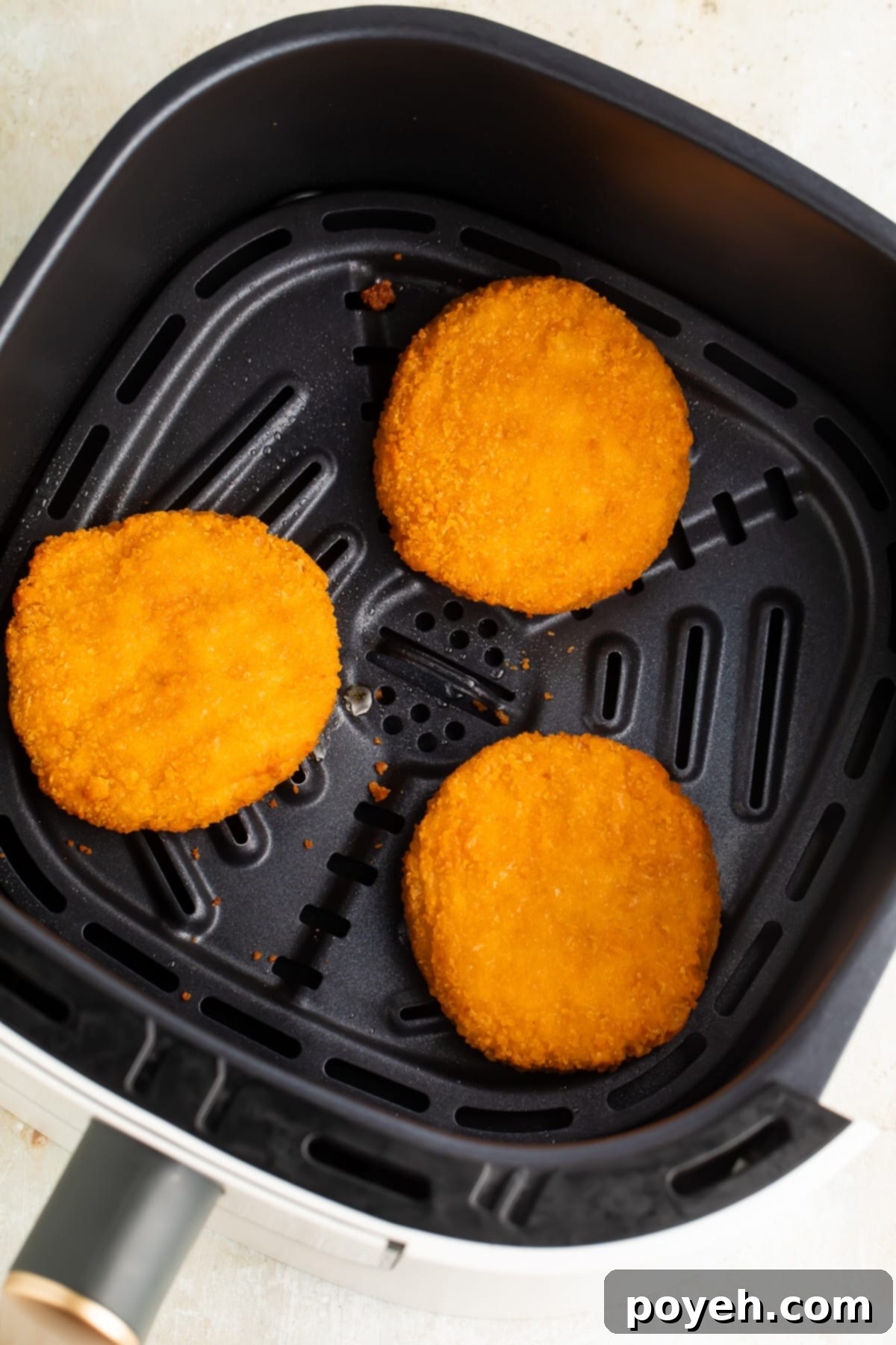 Three chicken patties in an air fryer basket.