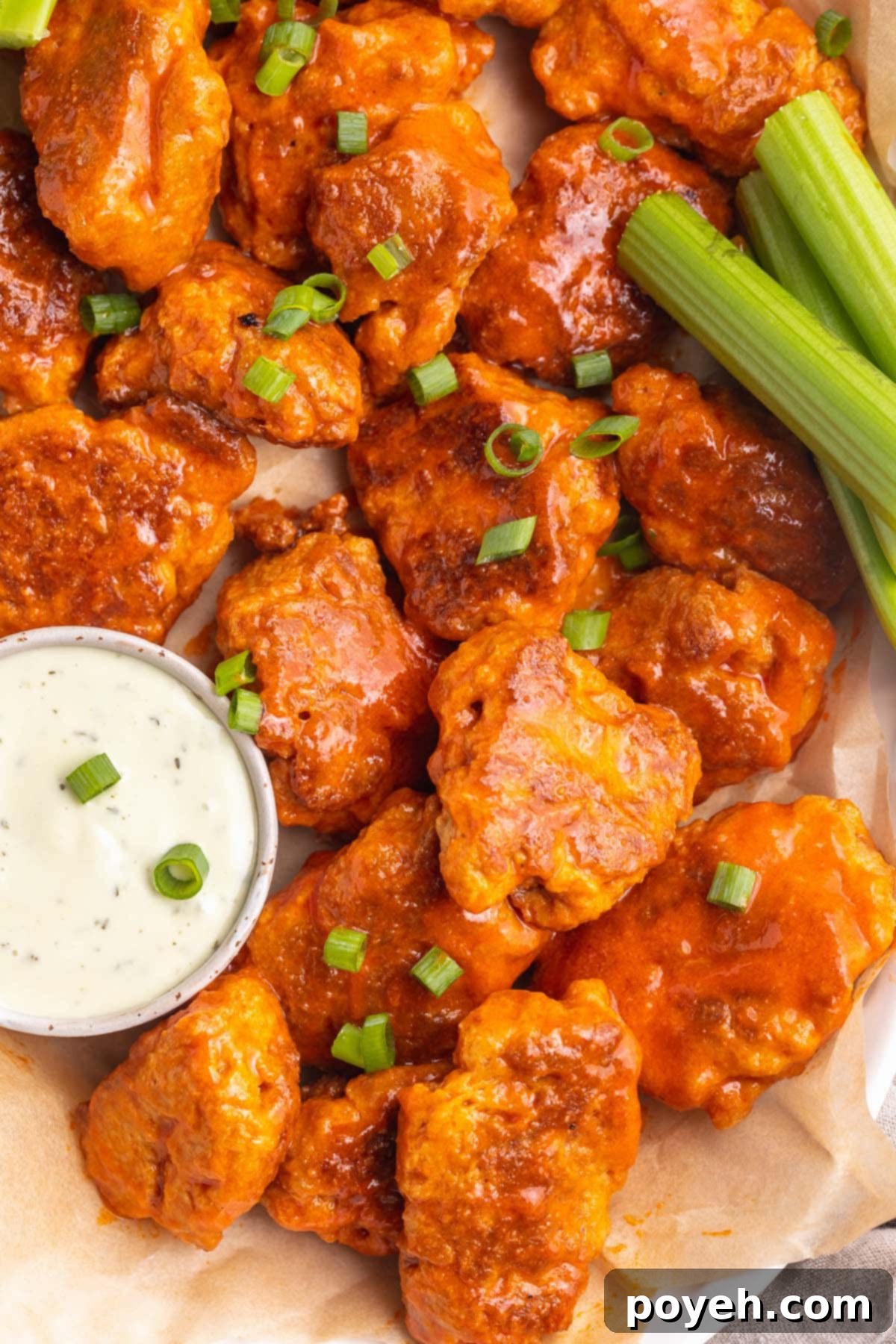 A platter of golden-brown, crispy vegan seitan buffalo wings, garnished with fresh celery sticks and a bowl of creamy ranch dressing for dipping. Perfect for any gathering.