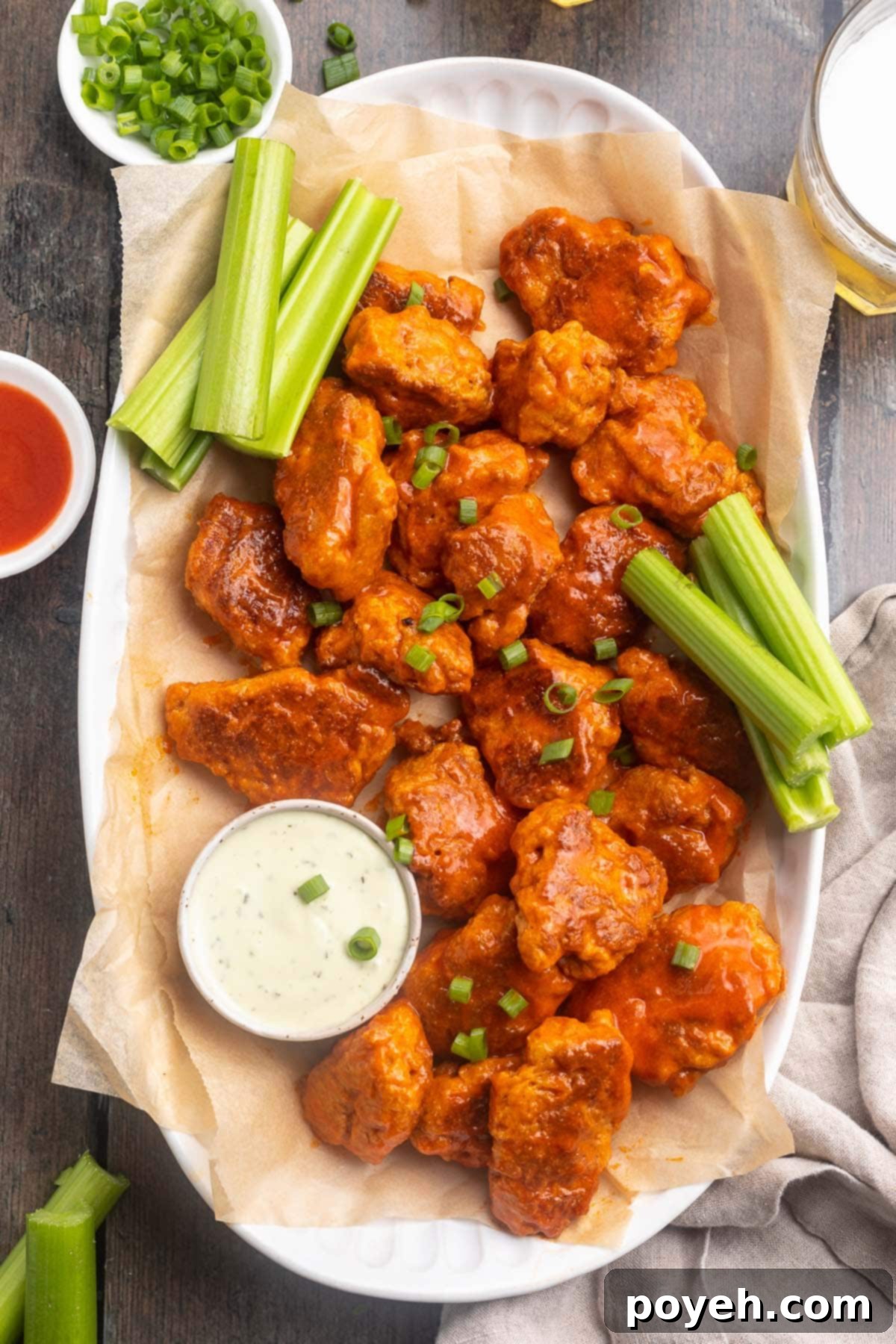 A vibrant close-up of a platter brimming with spicy buffalo-sauced seitan wings, accompanied by refreshing celery sticks and a small bowl of creamy vegan ranch dressing.