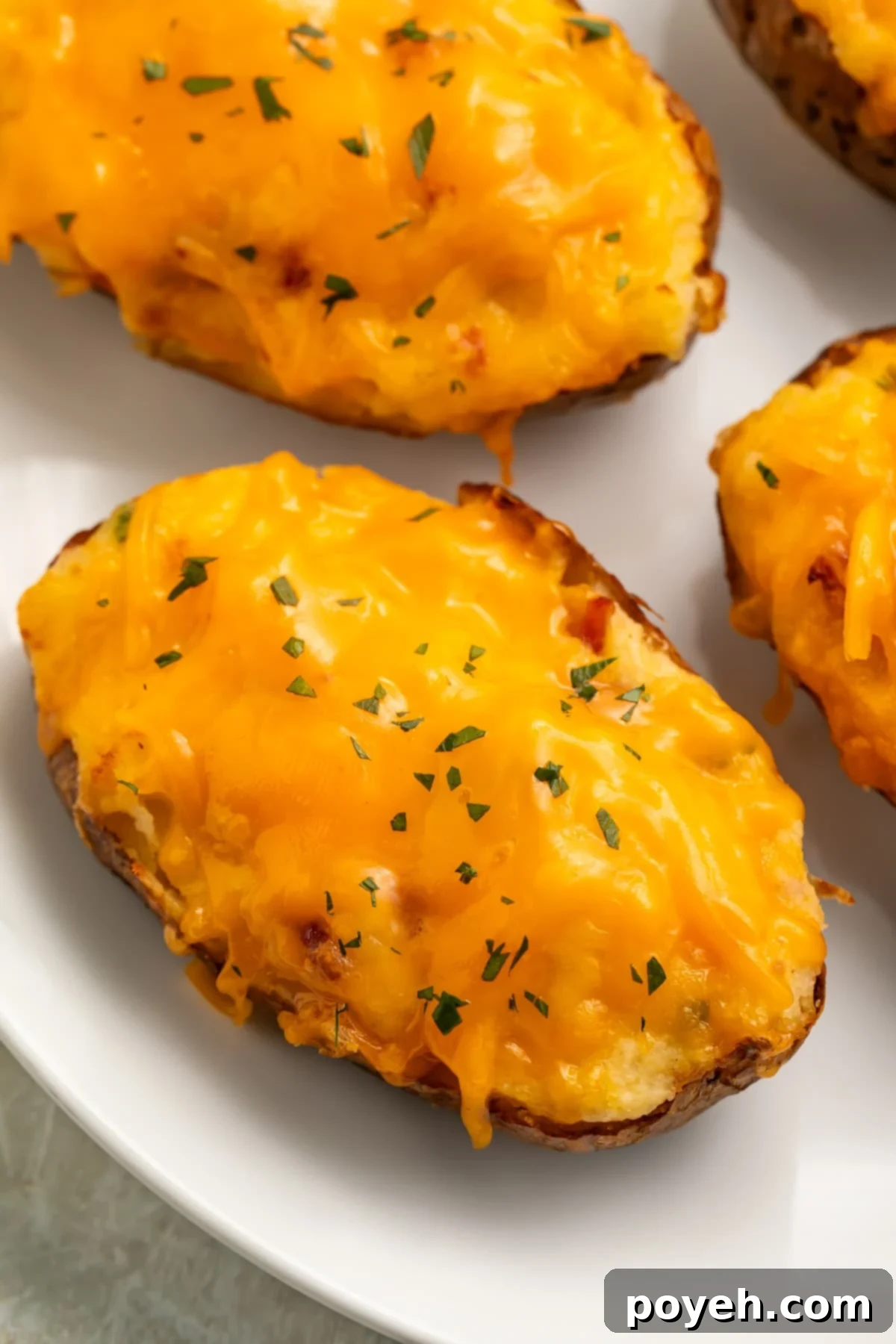 Air fryer twice baked potatoes topped with melty cheddar cheese and a garnish of chives on a white plate.