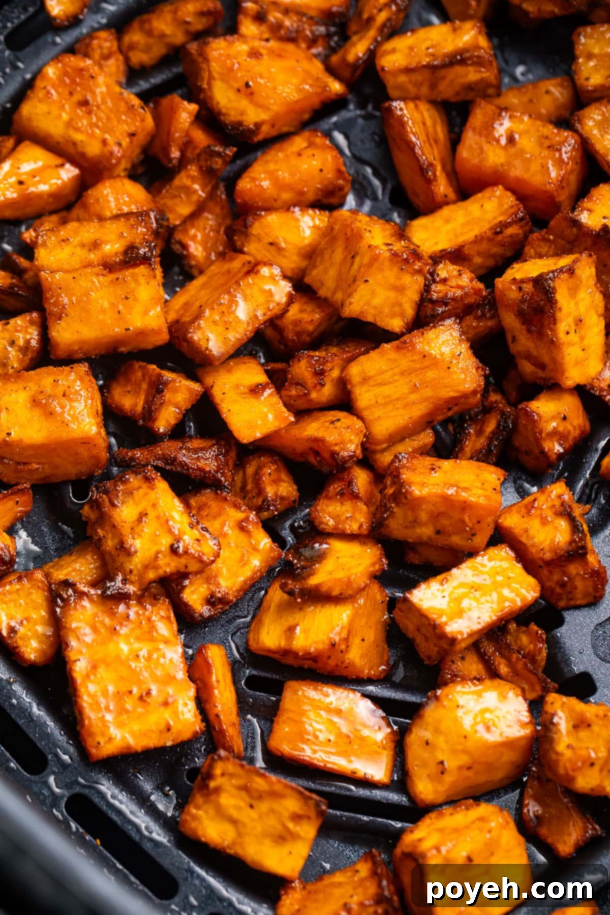 Crispy, golden-brown sweet potato cubes cooling in an air fryer basket after cooking.