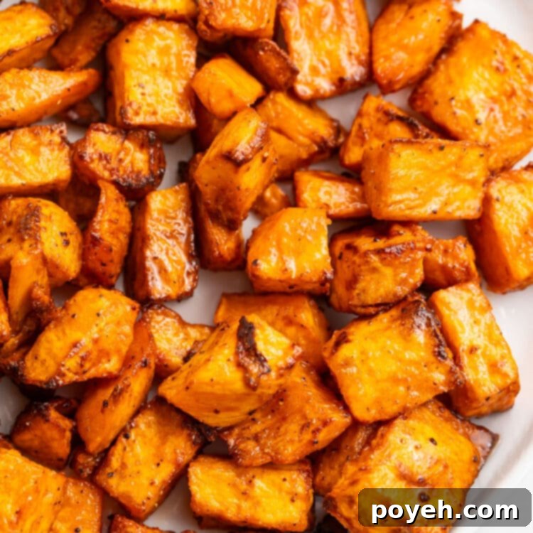 Air fryer sweet potato cubes served on a white plate with fresh herbs as garnish.