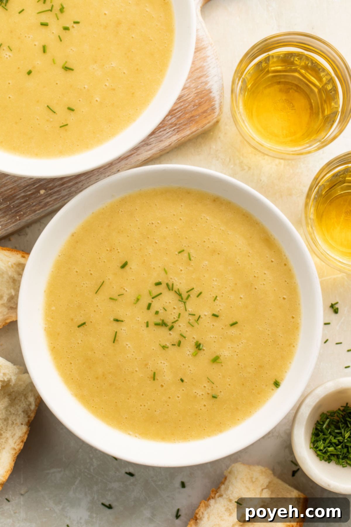 Two cozy bowls of creamy Instant Pot Potato Leek Soup, garnished with fresh chives, and surrounded by slices of rustic bread.