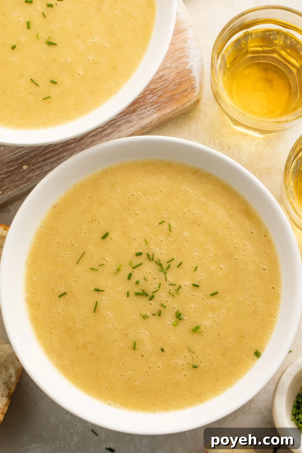 A close-up shot of creamy Instant Pot Potato Leek Soup in a rustic ceramic bowl, garnished with a sprinkle of fresh green chives, and served with a side of crusty bread.