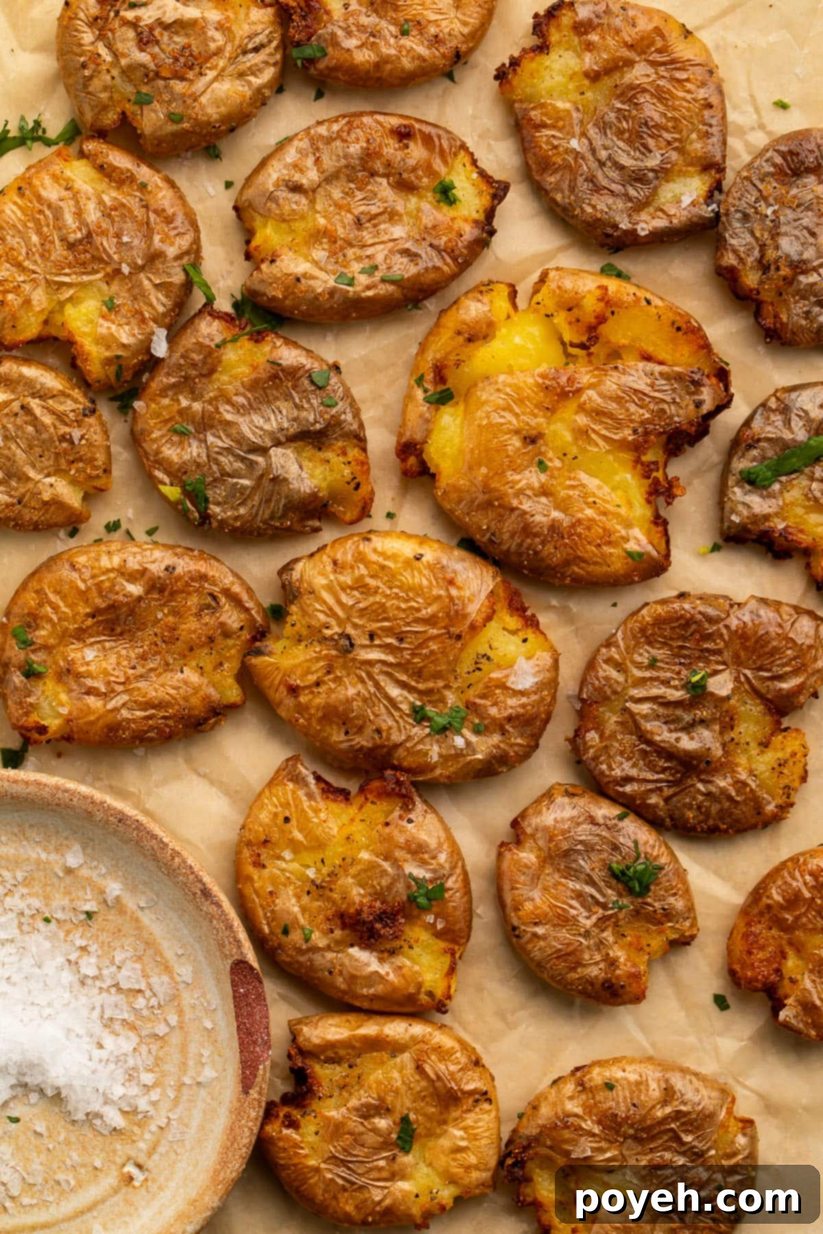 Crispy golden smashed potatoes, fresh from the air fryer, arranged artfully on parchment paper next to a small bowl of coarse sea salt, ready to be served.