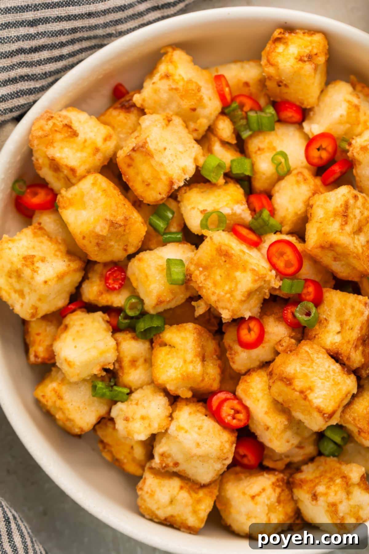 A bowl of crispy fried salt & pepper tofu with vibrant green onions and fiery red chilies, ready to be enjoyed.