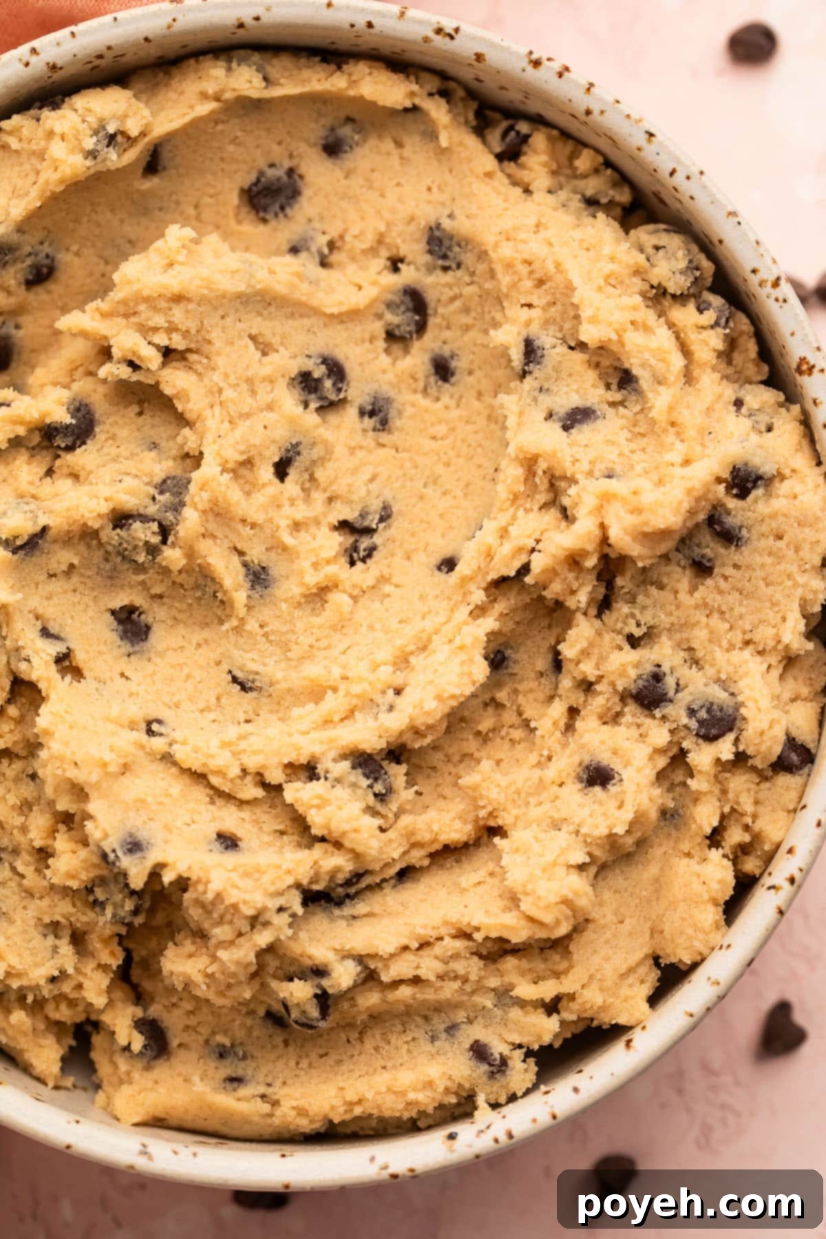 Gluten free cookie dough in a large white bowl surrounded by mini chocolate chips and a pink napkin.