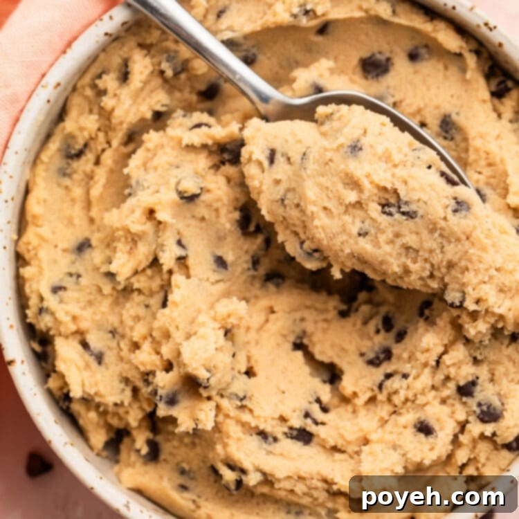 Gluten free cookie dough in a large white bowl with a spoon, surrounded by mini chocolate chips and a pink napkin.