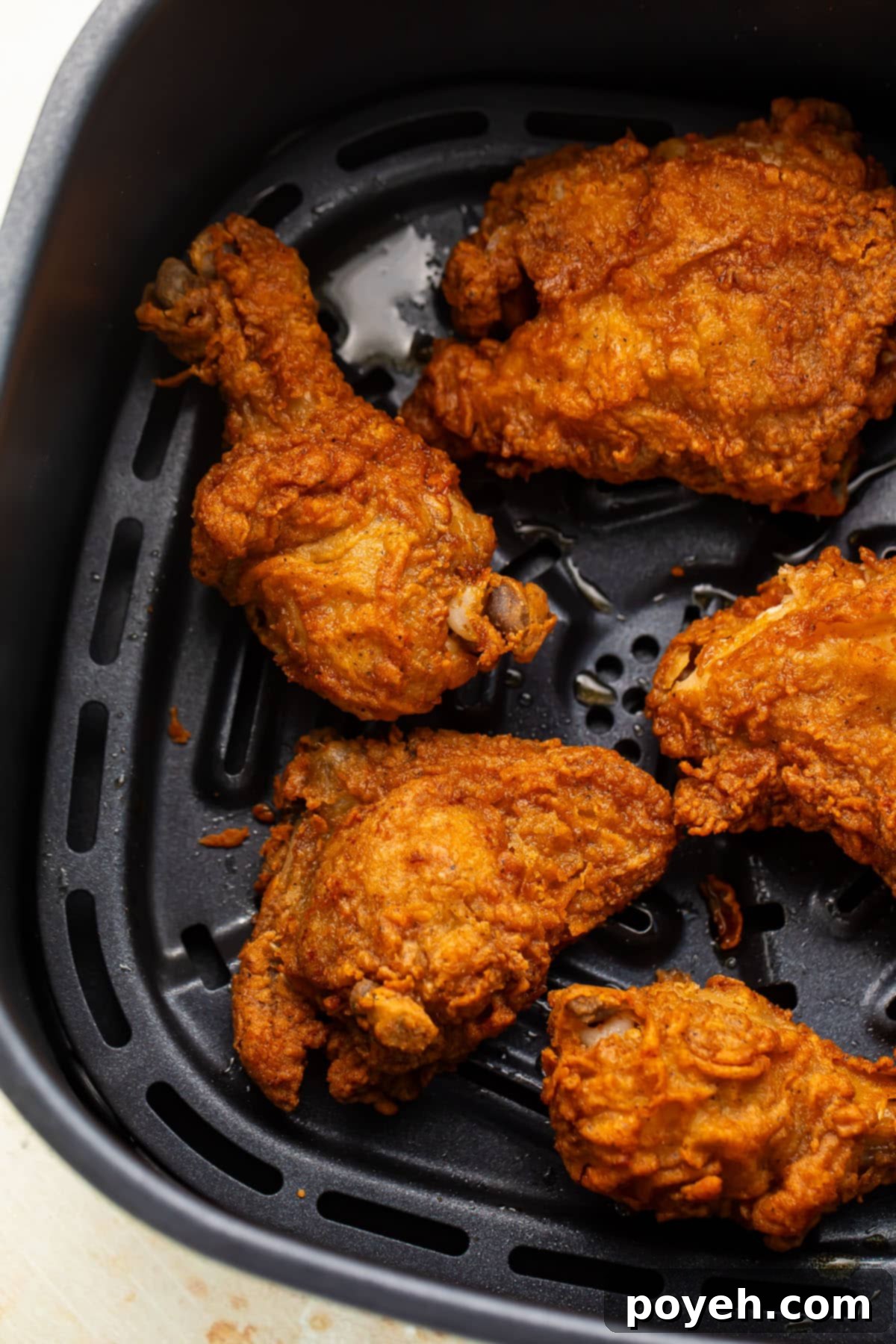 Crispy reheated fried chicken legs, thighs, and breasts in an air fryer basket, perfectly golden brown.