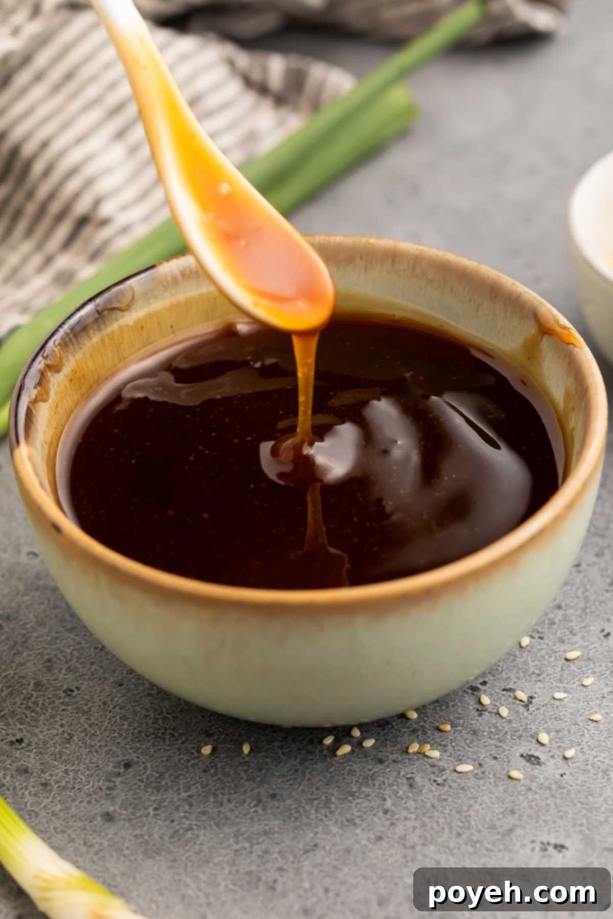 Gluten free teriyaki sauce being poured off a small white spoon into a bowl of teriyaki sauce.