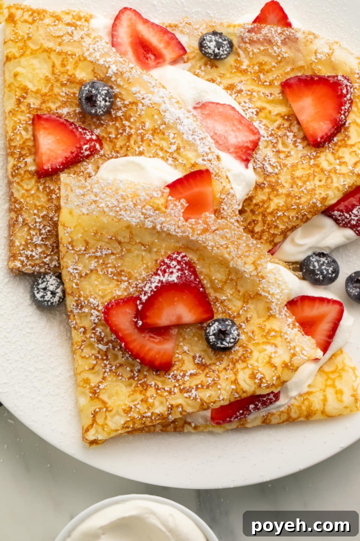 Close up of a gluten free crepe on a plate with fresh blueberries and sliced strawberries, demonstrating a delightful presentation.