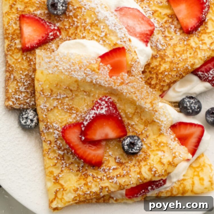 Close up of a gluten free crepe on a plate with fresh blueberries and sliced strawberries.