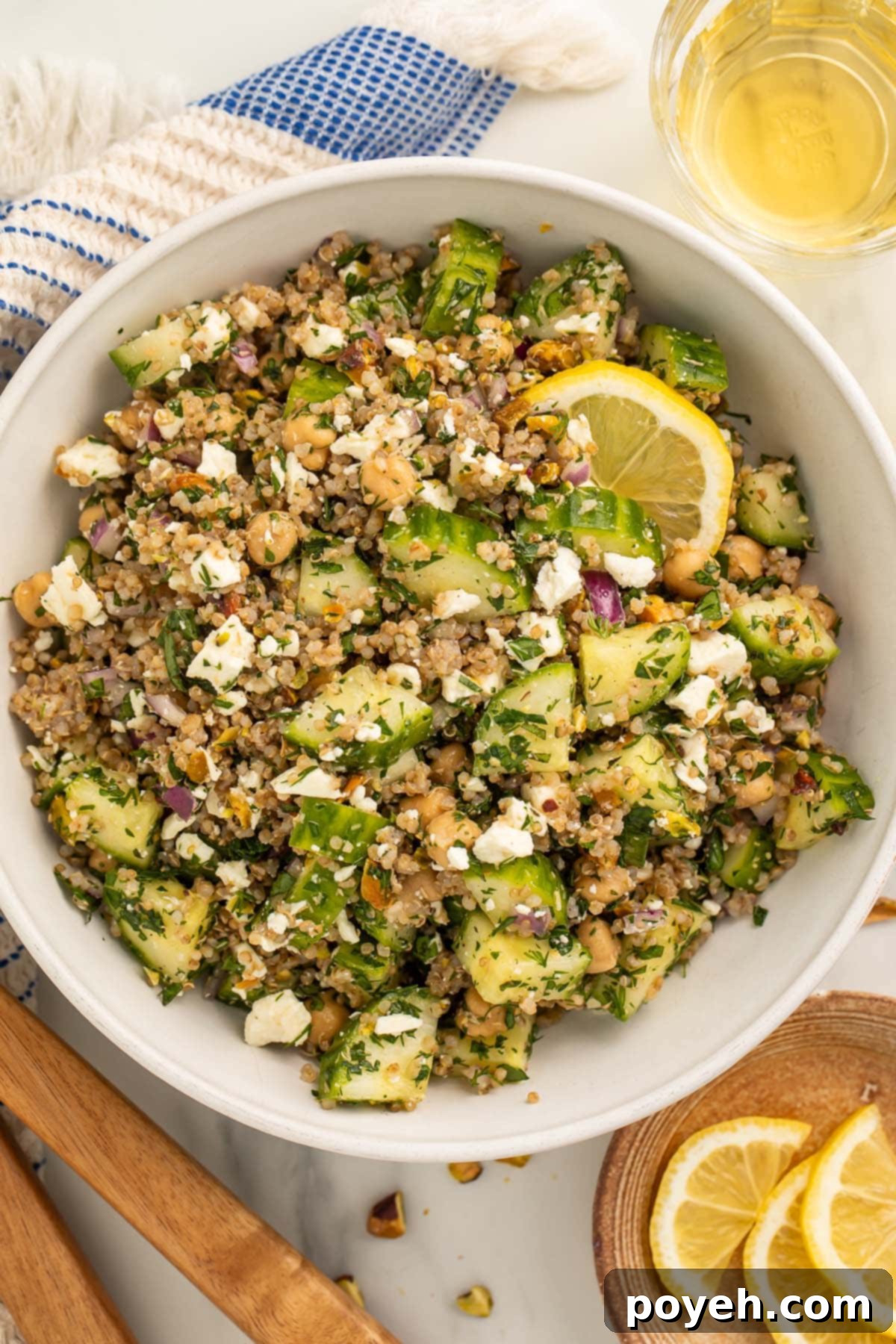 A close-up shot of the vibrant Jennifer Aniston salad, showcasing the rich textures and colors of quinoa, chickpeas, cucumber, pistachios, feta, and fresh herbs, ready to be enjoyed. Slices of fresh lemon are visible in the background.