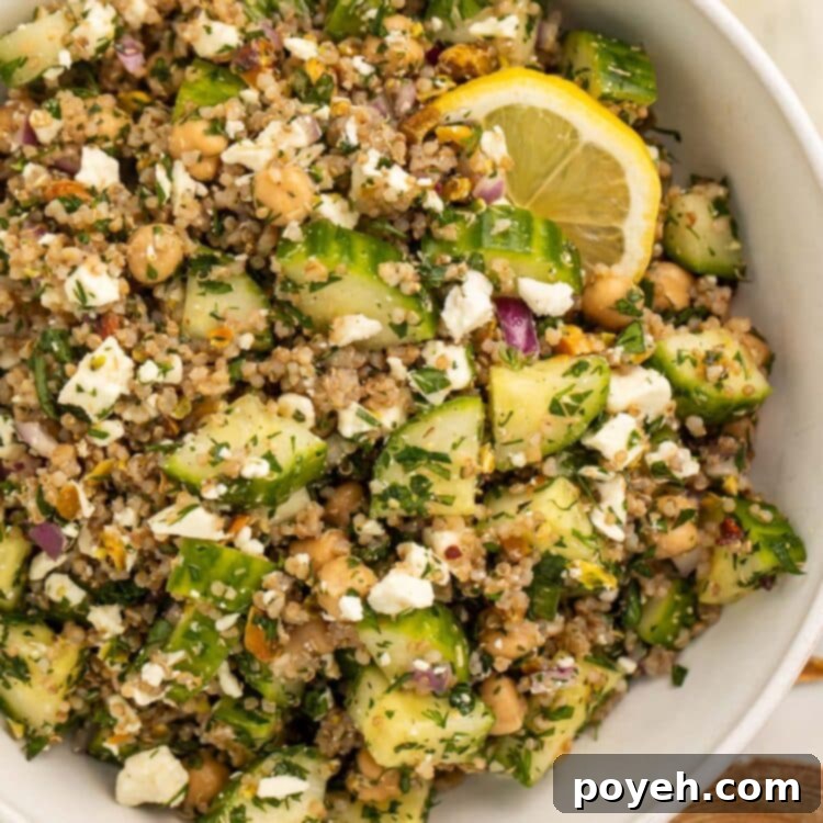The viral Jennifer Aniston salad (quinoa, chickpeas, cucumber, pistachios, feta, and herbs) in a large white bowl with slices of fresh lemon.