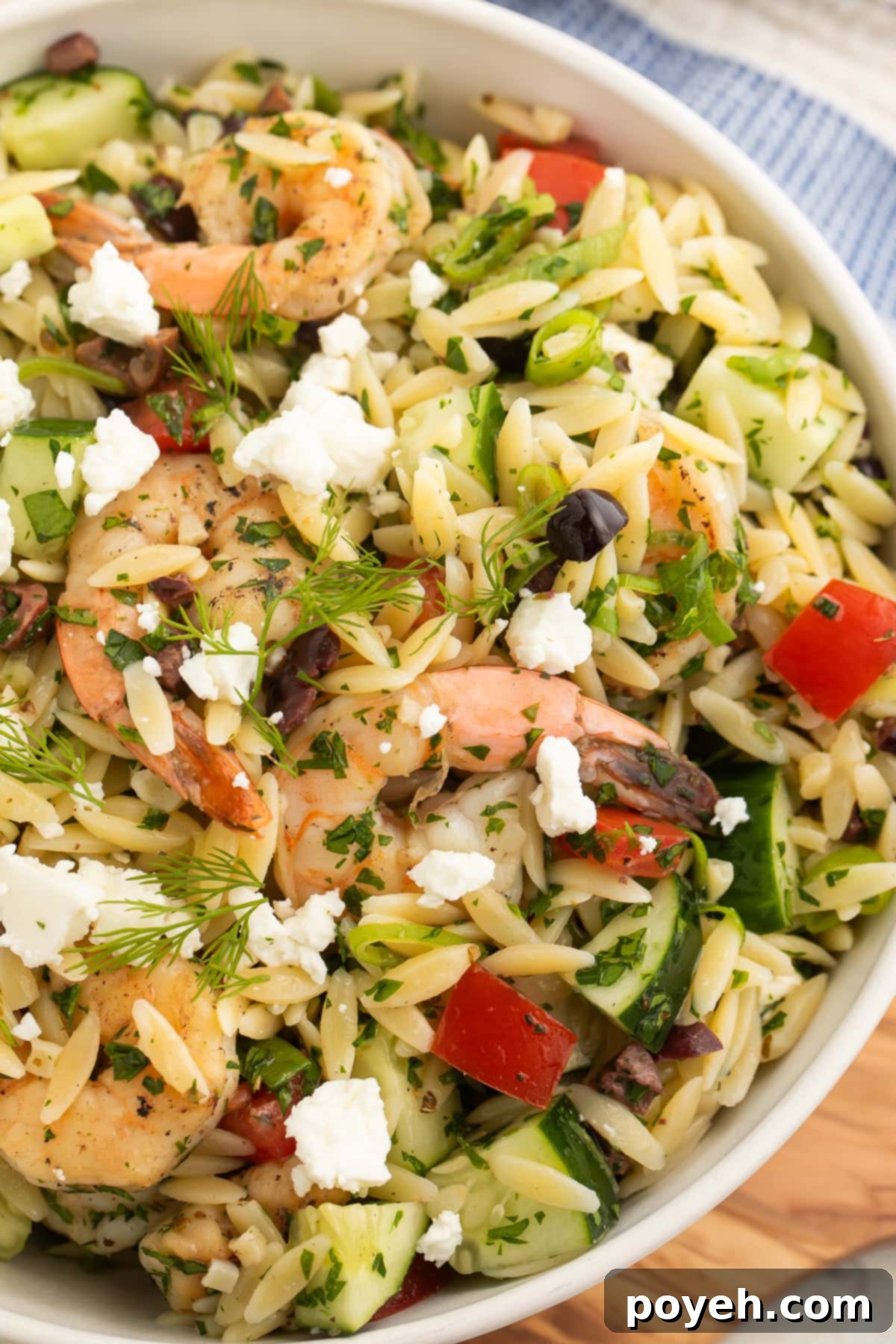 Close-up of a bowl of Greek shrimp salad with orzo, highlighting the vibrant colors and fresh ingredients like shrimp, feta, olives, and herbs.
