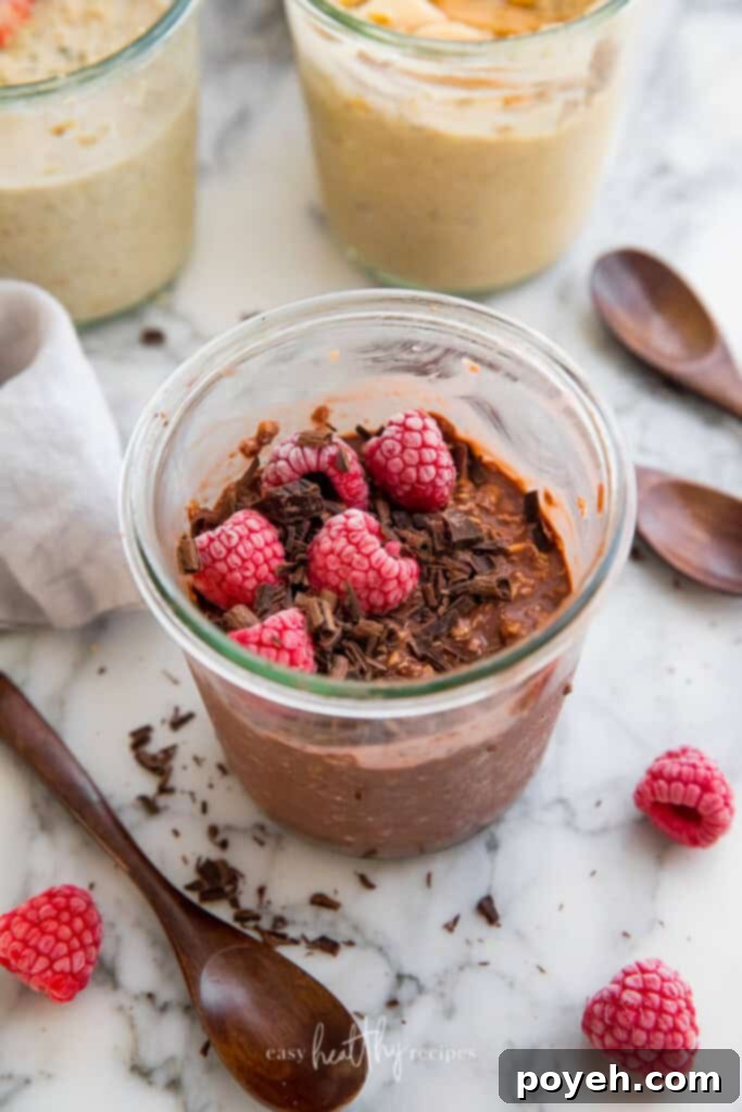 A jar of rich chocolate vegan overnight oats, elegantly topped with delicate chocolate shavings and bright red raspberries, creating a decadent and inviting breakfast.