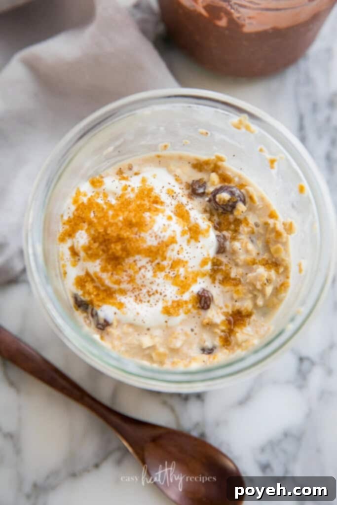 A jar of cinnamon raisin vegan overnight oats, artfully topped with a dollop of yogurt, a dusting of brown sugar, plump raisins, and a sprinkle of cinnamon, presenting a comforting and flavorful breakfast.