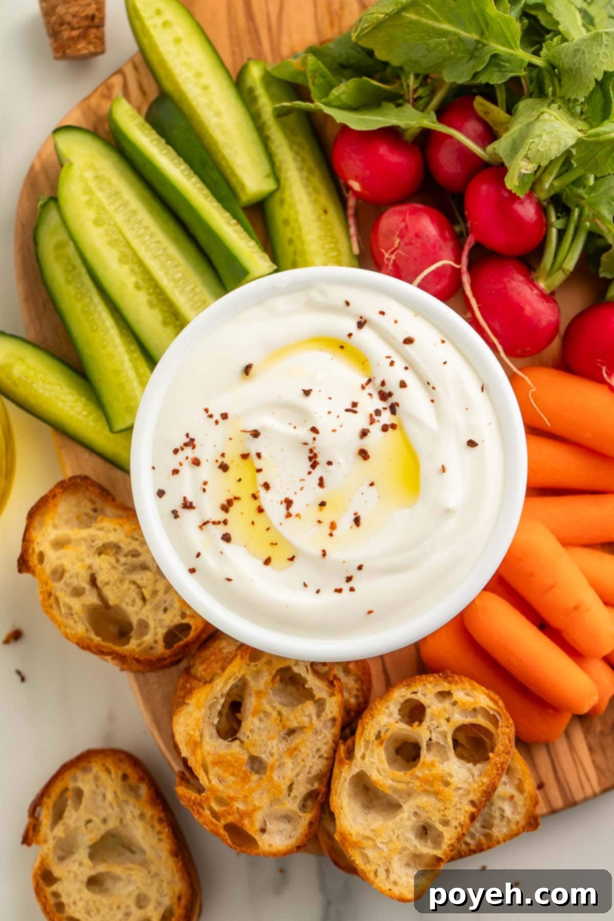 A bowl of savory whipped cottage cheese resting on a wooden board, surrounded by crostini, pickles, carrot sticks, and radishes, ready to be served.