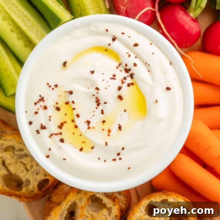 A bowl of savory whipped cottage cheese resting on a wooden board, surrounded by crostini, pickles, carrot sticks, and radishes, illustrating the recipe result.