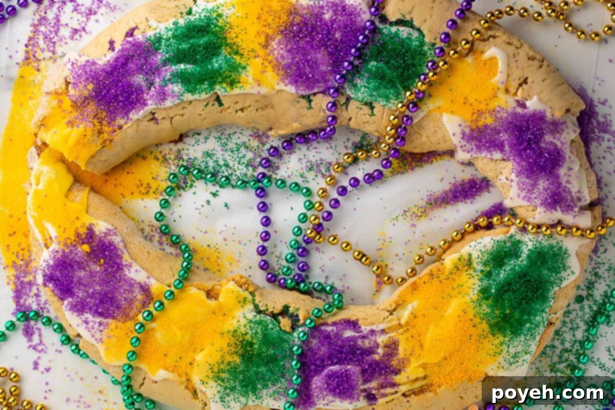 A large oval-shaped gluten free king cake topped with purple, yellow, and green sanding sugar and surrounding by purple, gold, and green Mardi Gras bead necklaces.