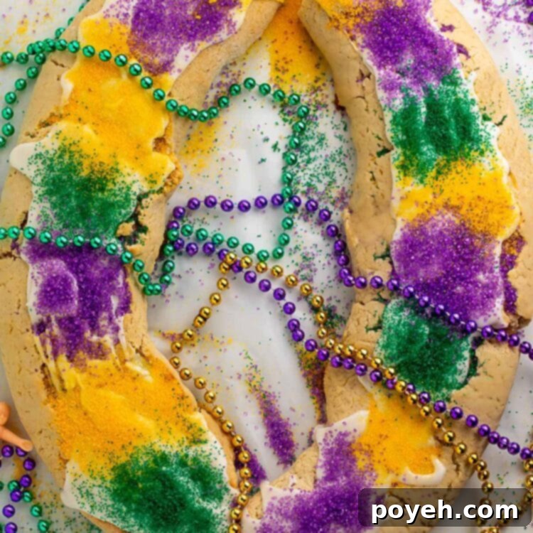 A large oval-shaped gluten free king cake topped with purple, yellow, and green sanding sugar and surrounding by purple, gold, and green Mardi Gras bead necklaces.