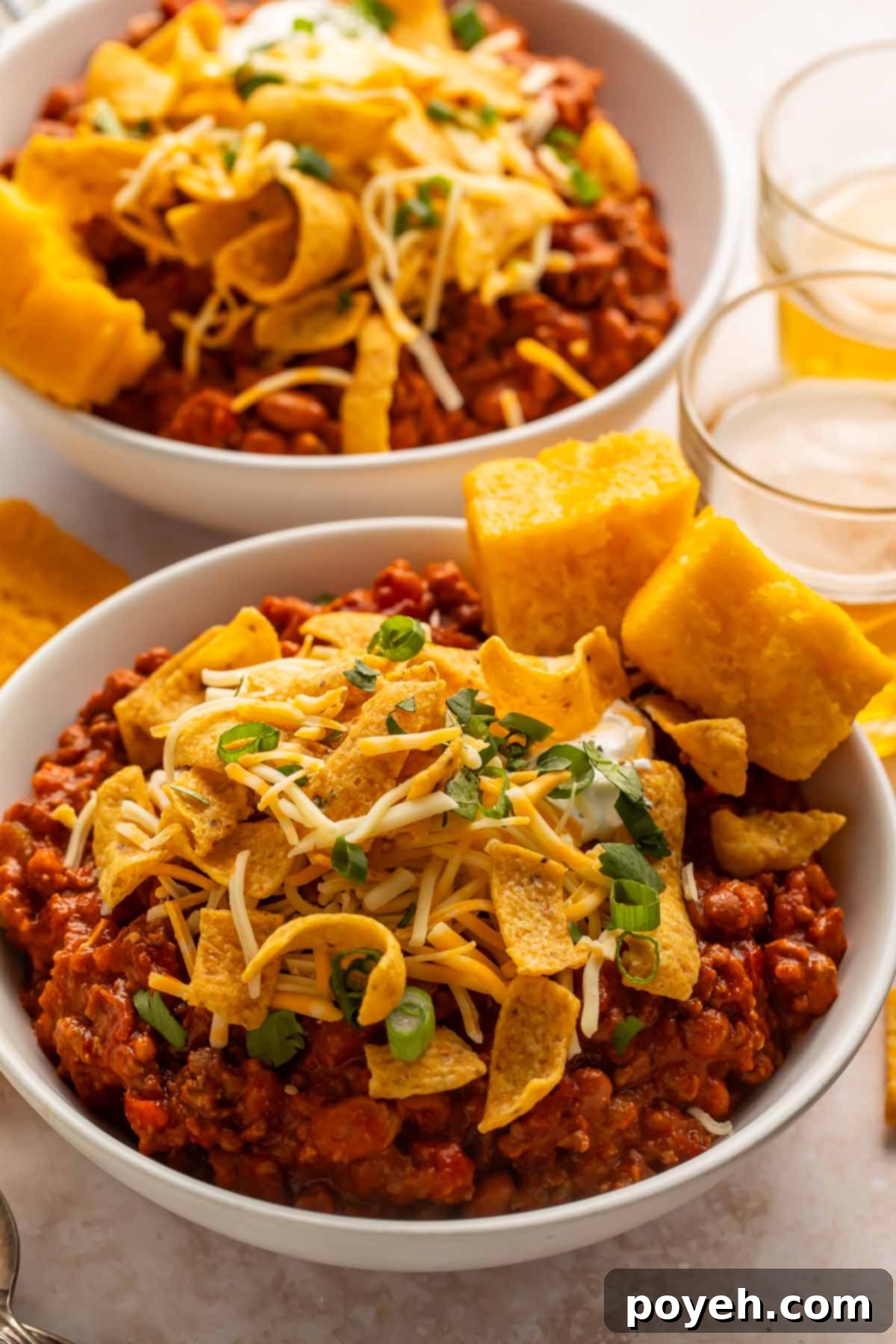 Two bowls of boilermaker chili topped with corn chips and two squares of cornbread, photographed from the side. The chili looks rich and hearty.