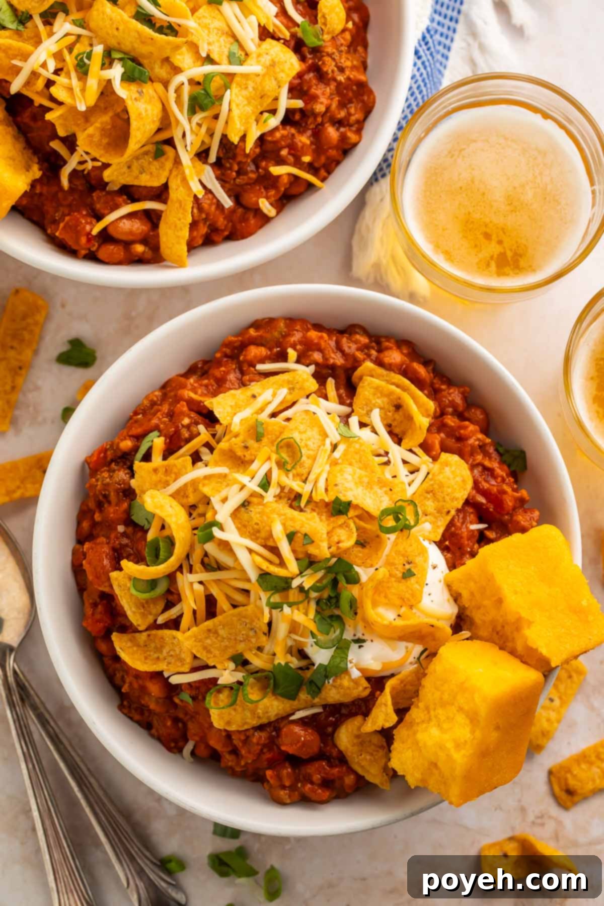 Two bowls of boilermaker chili topped with corn chips and two squares of cornbread, photographed from above. The vibrant colors and textures are appealing.