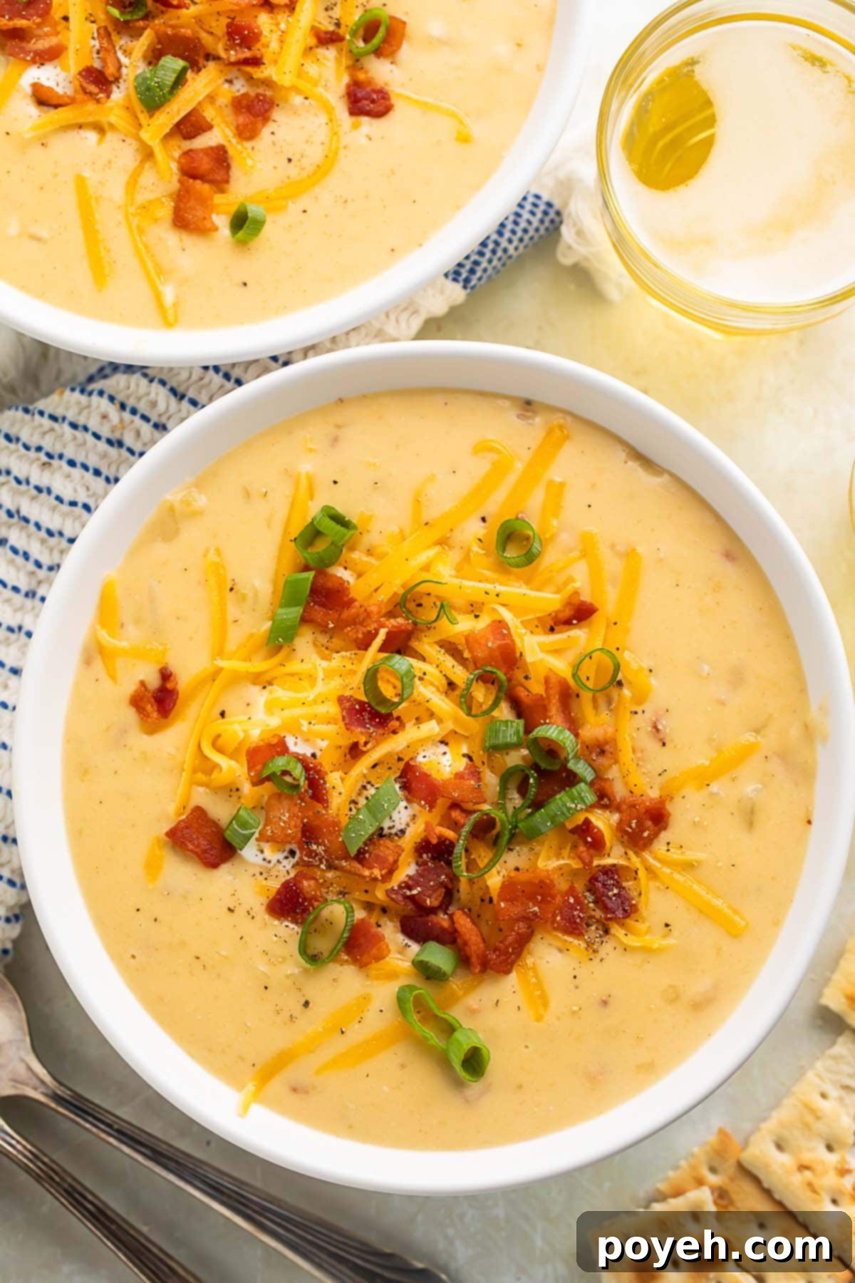 Two bowls of gluten free potato soup topped with chopped bacon, shredded cheese, and sliced green onions.