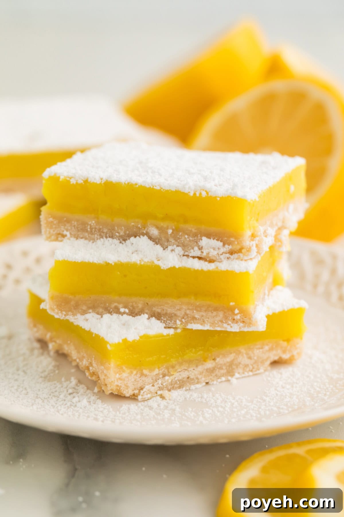 A stack of 3 vegan lemon bars, each topped with powdered sugar, on a white plate.