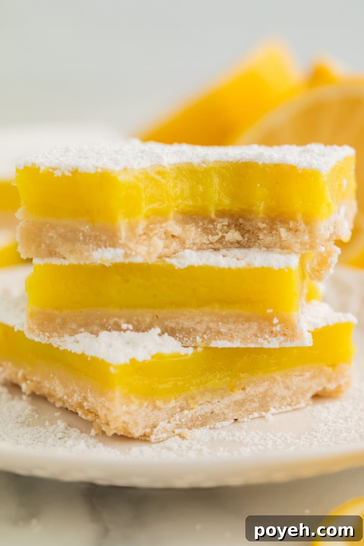 A stack of 3 vegan lemon bars, each topped with powdered sugar, on a white plate.