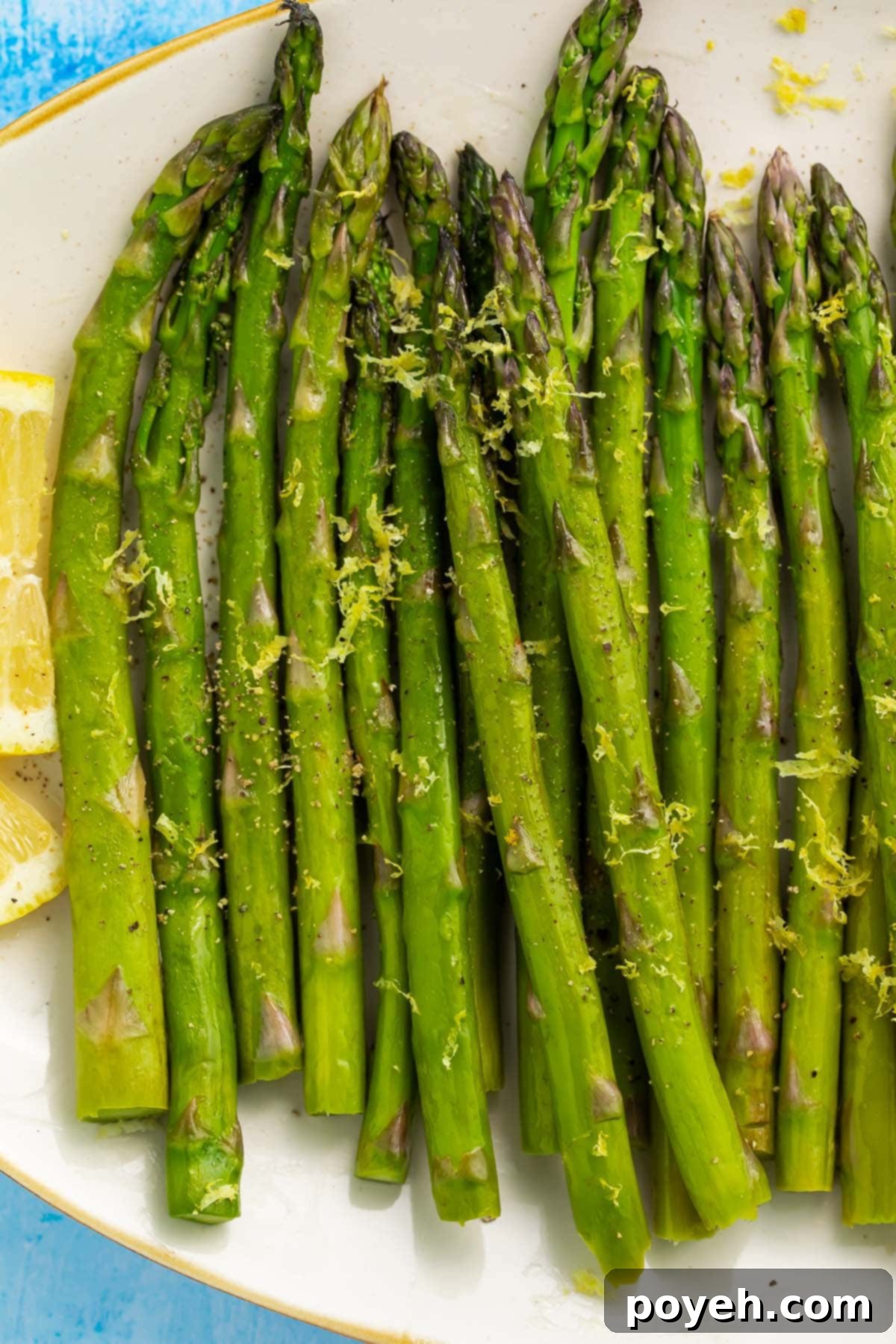 Asparagus, cooked in a sous vide, arranged on a white oval platter on a blue background.