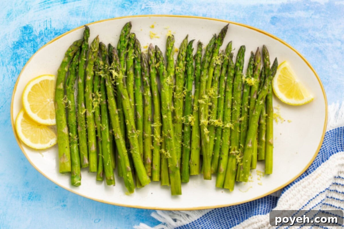 Several stalks of sous vide asparagus arranged in a row on an oval platter, with lemon coins to garnish.