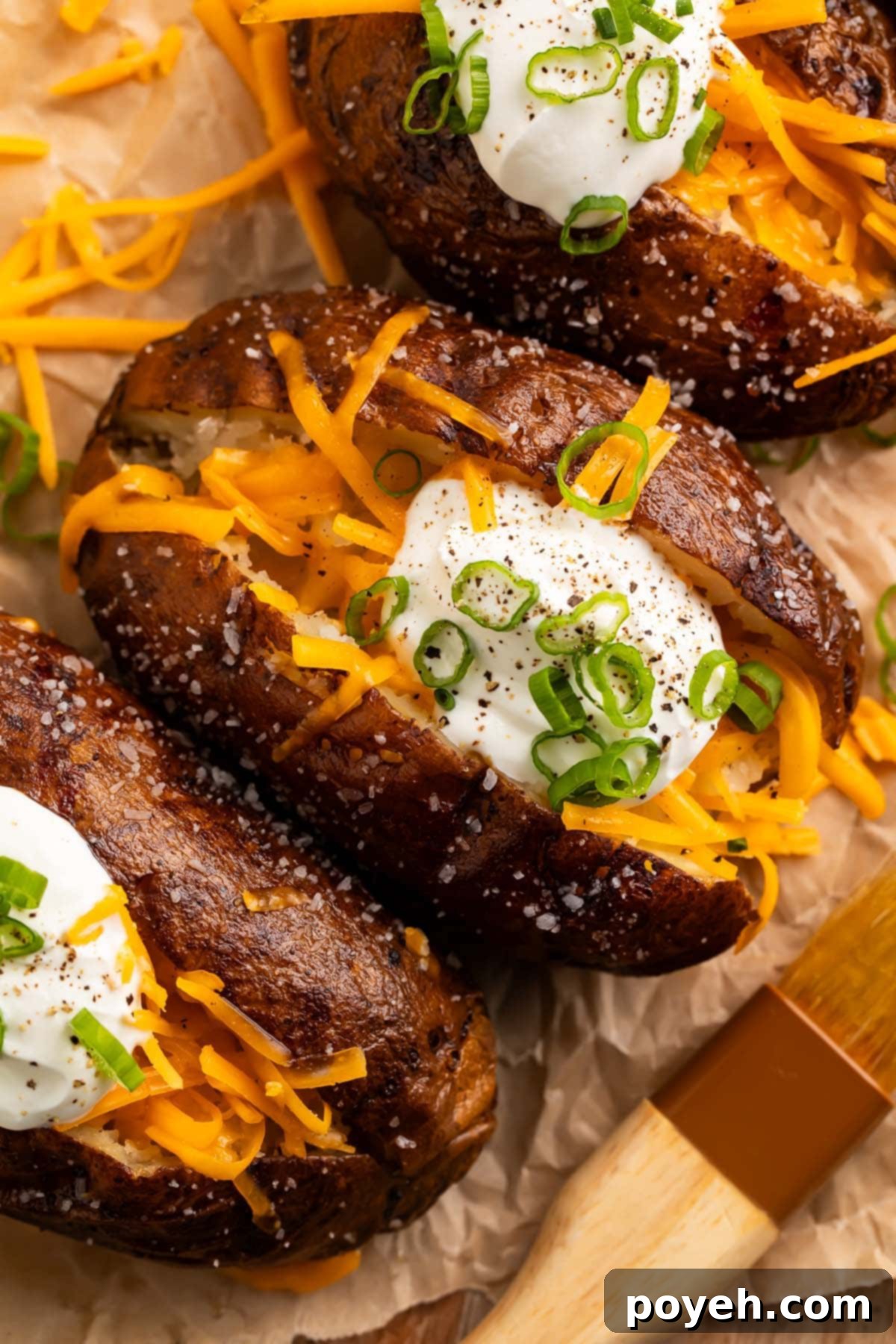 Smoked potatoes, split open and topped with shredded cheddar cheese, a dollop of sour cream, and thinly sliced green onions.