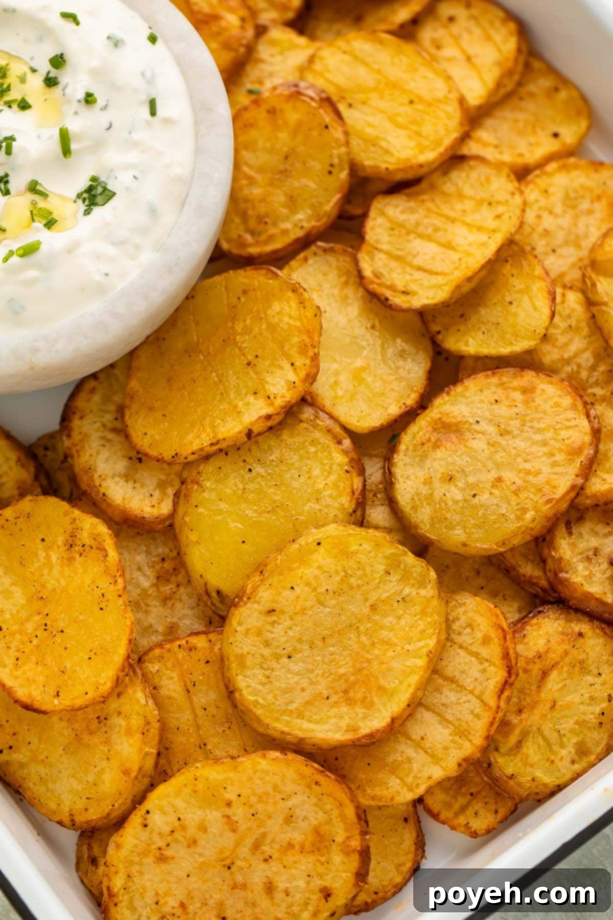 Irresistible Air Fryer Potatoes with Creamy Herb Sauce 2 Close-up of thinly sliced potatoes, cooked to golden perfection in the air fryer, served on a rustic tray alongside a small bowl of creamy dipping sauce, garnished with fresh herbs.