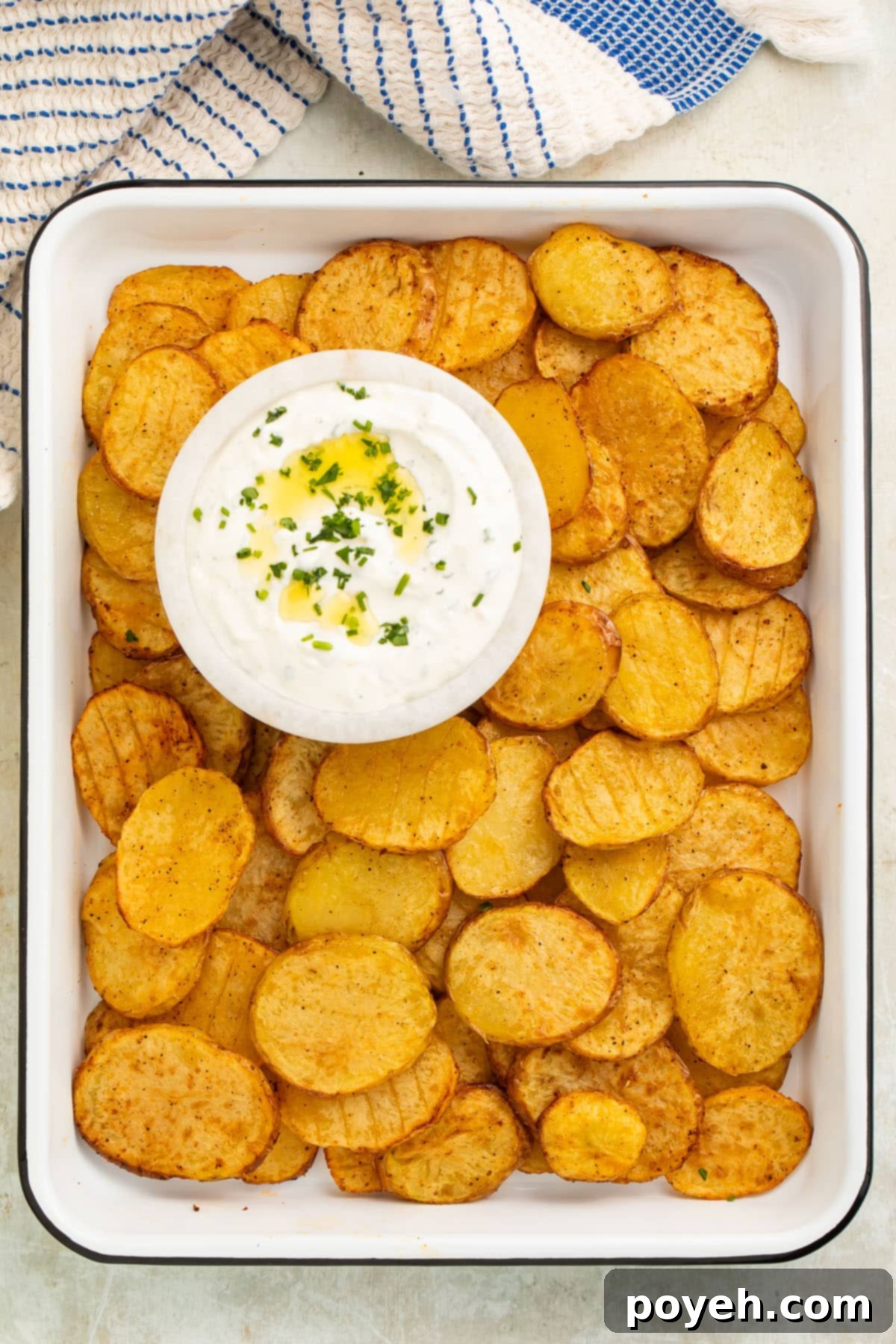 Irresistible Air Fryer Potatoes with Creamy Herb Sauce 3 Thinly sliced potatoes, cooked to a perfect golden crisp in the air fryer, displayed on a serving tray with a refreshing bowl of creamy dill sauce for dipping.