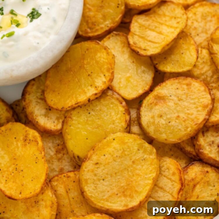 Irresistible Air Fryer Potatoes with Creamy Herb Sauce 4 Close-up of thinly sliced potatoes, cooked to golden perfection in the air fryer, served on a rustic tray alongside a small bowl of creamy dipping sauce, garnished with fresh herbs.