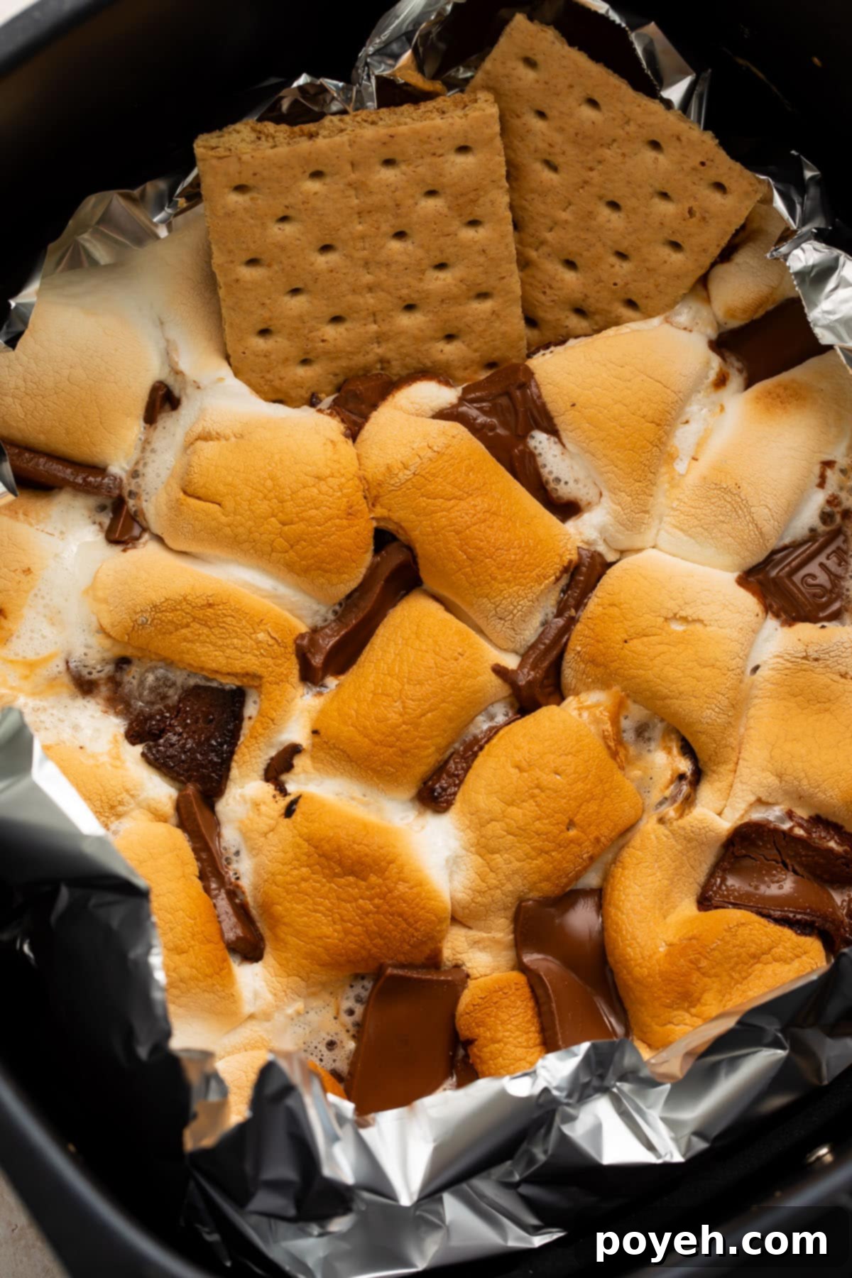 Gooey air fryer s'mores dip in an air fryer basket, lined with aluminum foil and ready to be served with graham crackers.