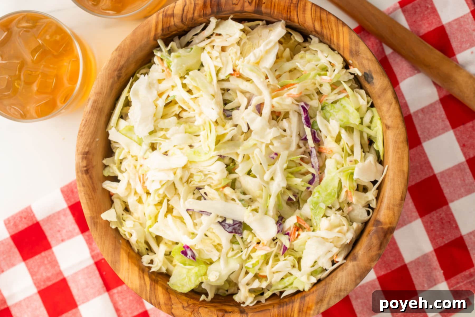 Creamy Plant-Based Slaw 3 A wooden bowl containing creamy vegan coleslaw sits on a table partially covered by a cheerful red and white checkerboard tablecloth.