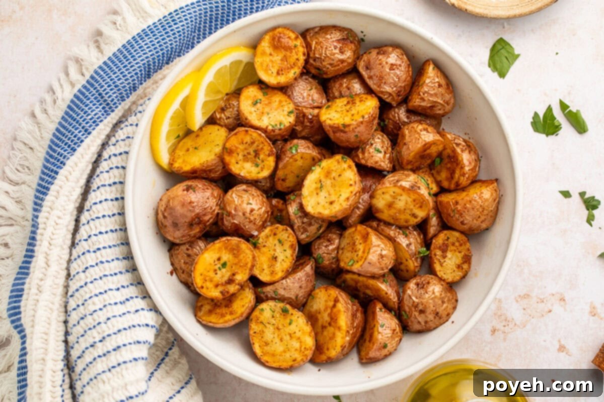A close-up of a bowl filled with perfectly cooked air fryer red potatoes, golden-brown and garnished with fresh parsley, sitting next to a blue striped kitchen towel.