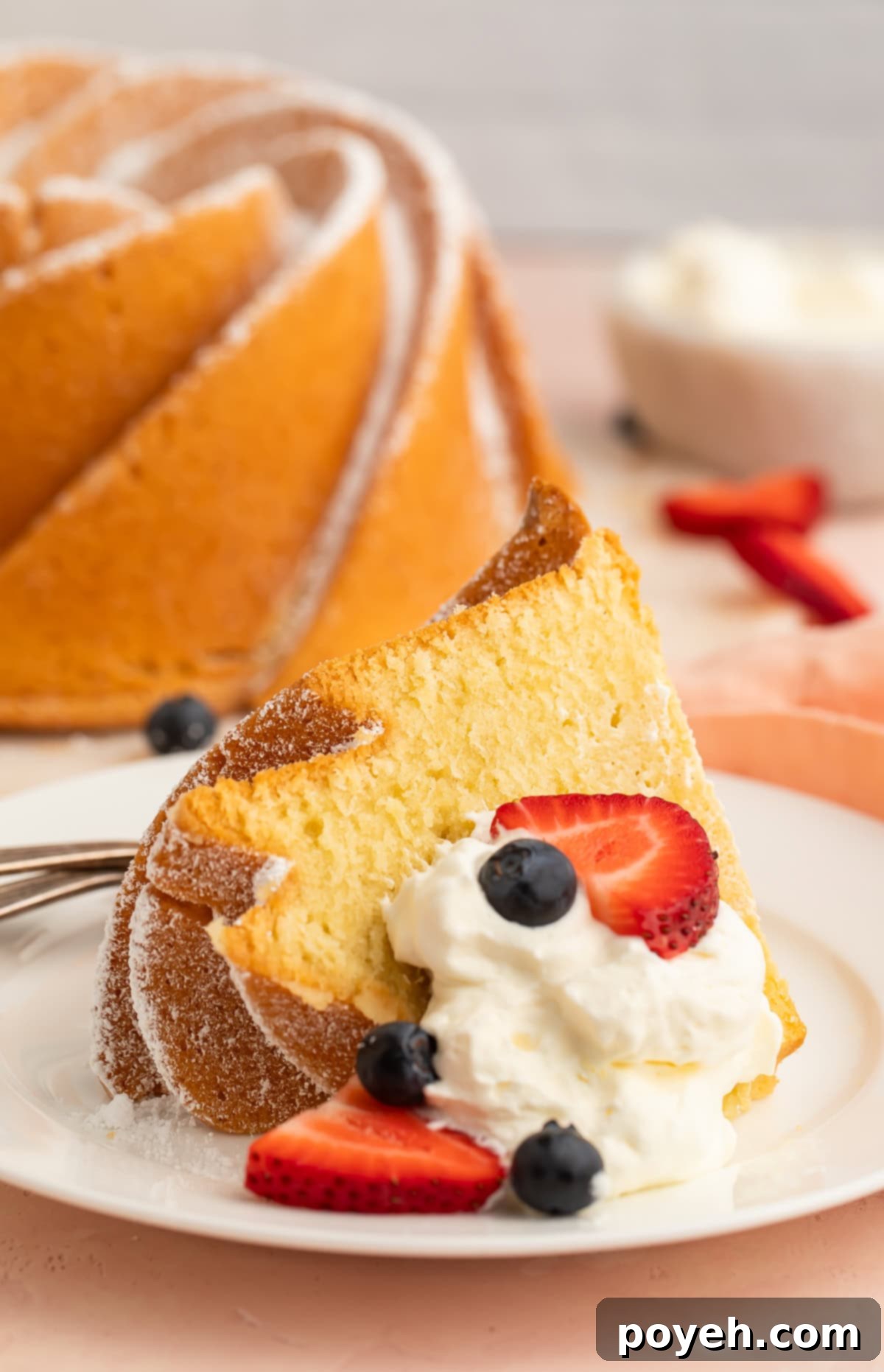 A beautifully sliced gluten-free pound cake on a dessert plate, adorned with fresh whipped cream and a medley of red berries.