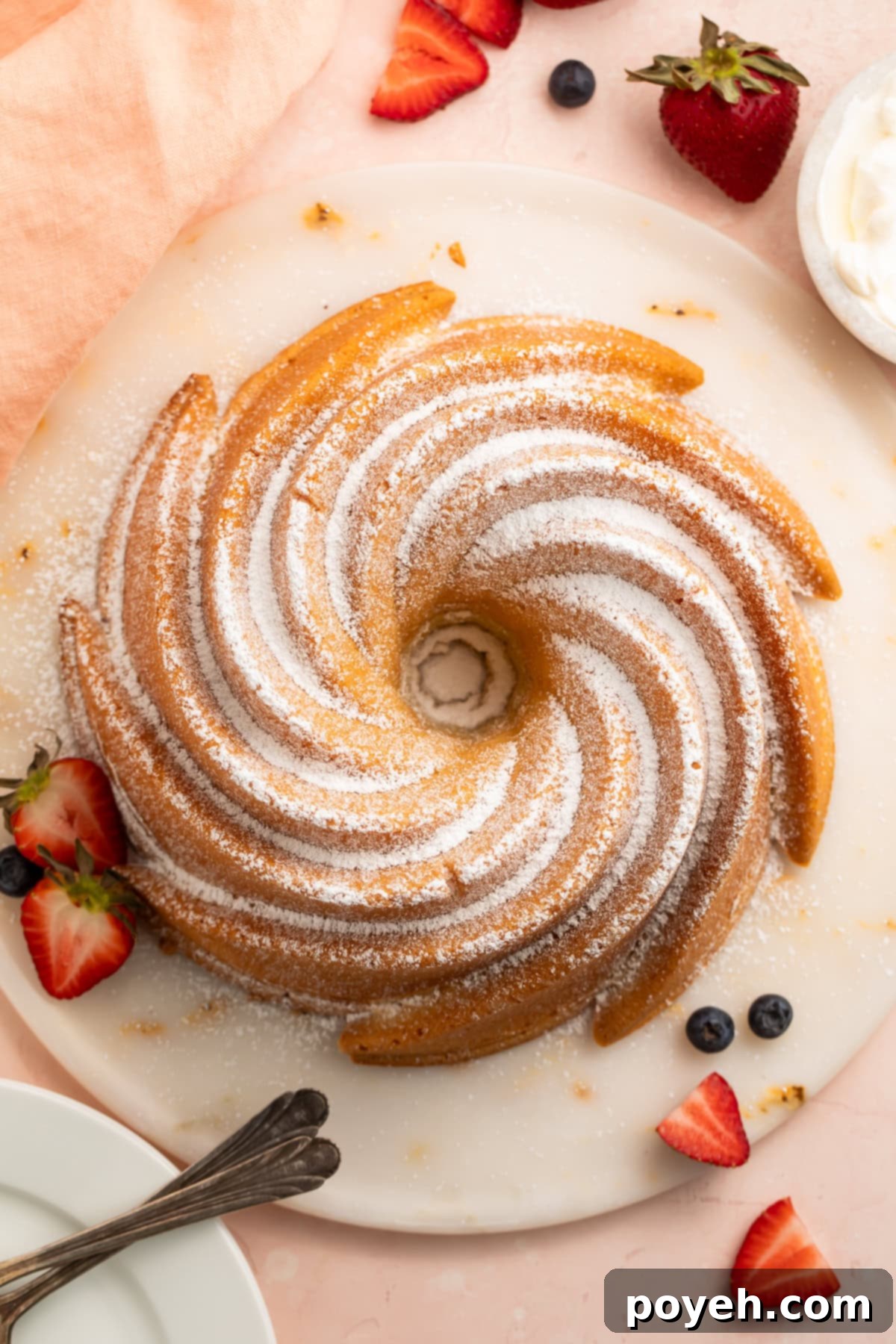 An overhead view of a golden-brown gluten-free pound cake, beautifully presented on a plate with fresh mixed berries.