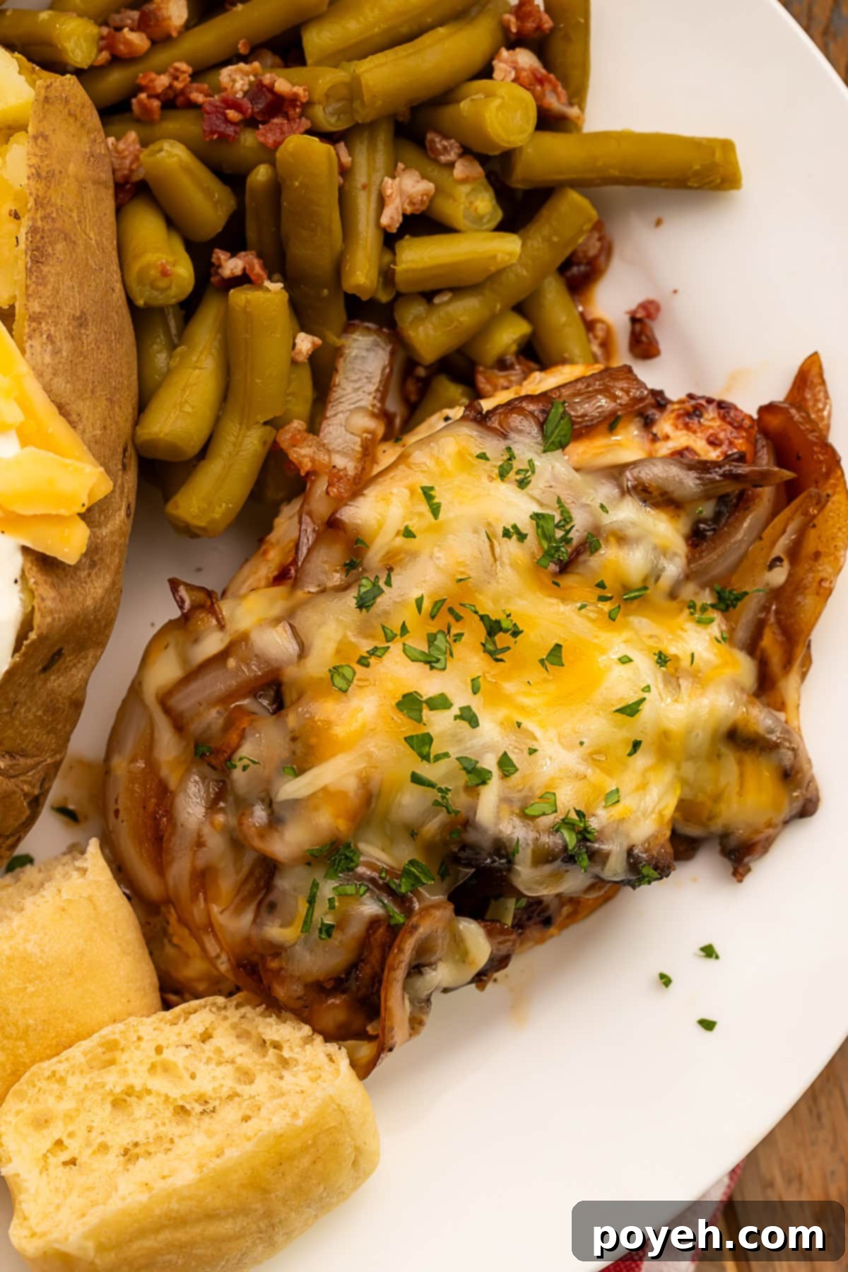 Smothered chicken breast topped with melted cheese served with a side of bacon green beans and a roll cut in half.