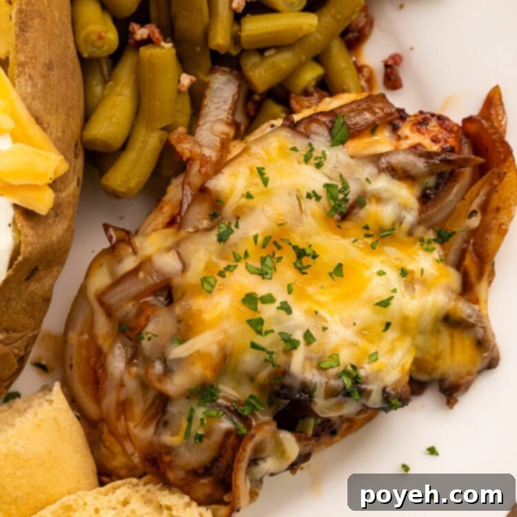 Smothered chicken breast topped with melted cheese served with a side of bacon green beans and a roll cut in half.