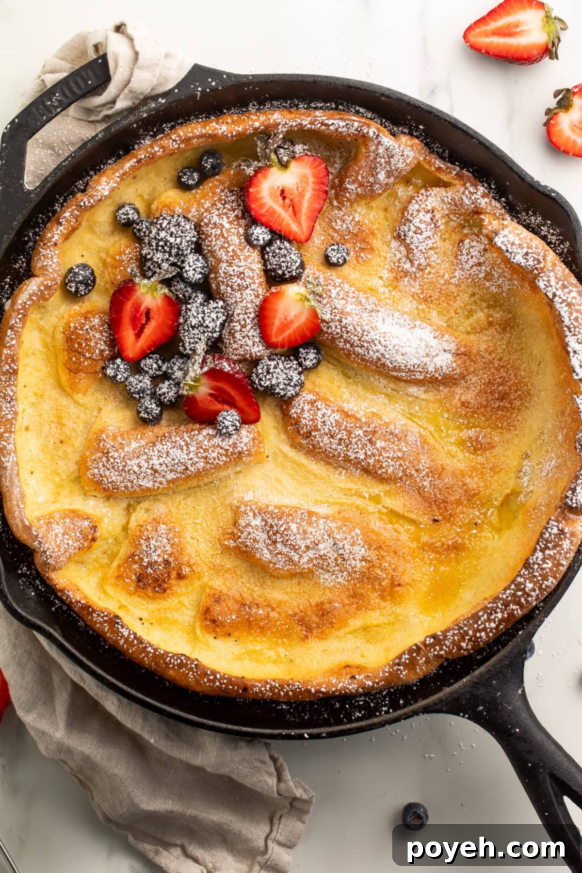 A stunning Gluten-Free Dutch Baby Pancake fresh from a cast iron skillet, lightly dusted with powdered sugar and adorned with vibrant fresh berries.